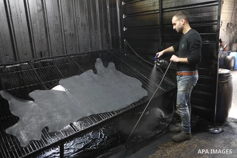 Palestinian workers paint leather and putting pieces out to dry as part of the finish process of leather tanning in a small factory to sell it to manufacture of shoes, in the West Bank city of Hebron on October 27, 2021....