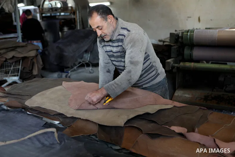 Palestinian workers paint leather and putting pieces out to dry as part of the finish process of leather tanning in a small factory to sell it to manufacture of shoes, in the West Bank city of Hebron on October 27, 2021....