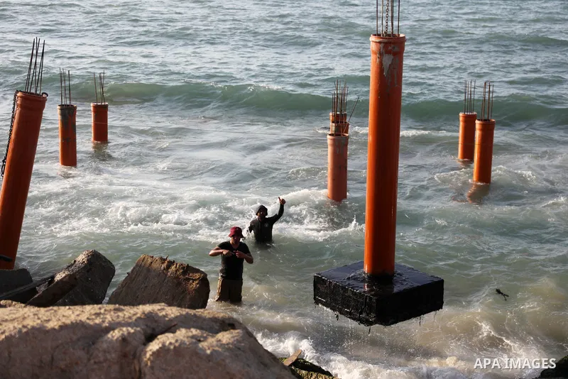 Palestinian workers operate a bulldozer to set up stilts in the Mediterranean sea to build a coffee shop at the Gaza city beach, using simple materials availabe in the besieged Gaza Strip, on October 27, 2021. Photo by M...