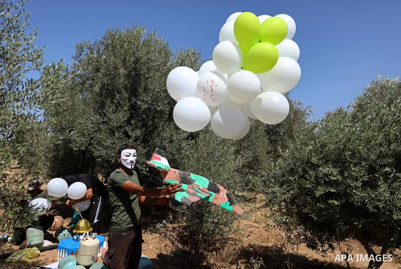 Masked Palestinians prepare incendiary balloons near Jabalia in the northern of Gaza Strip, on September 4, 2021. Reports in Palestinian media indicated that units in charge of incendiary balloon attacks on Israeli plann...