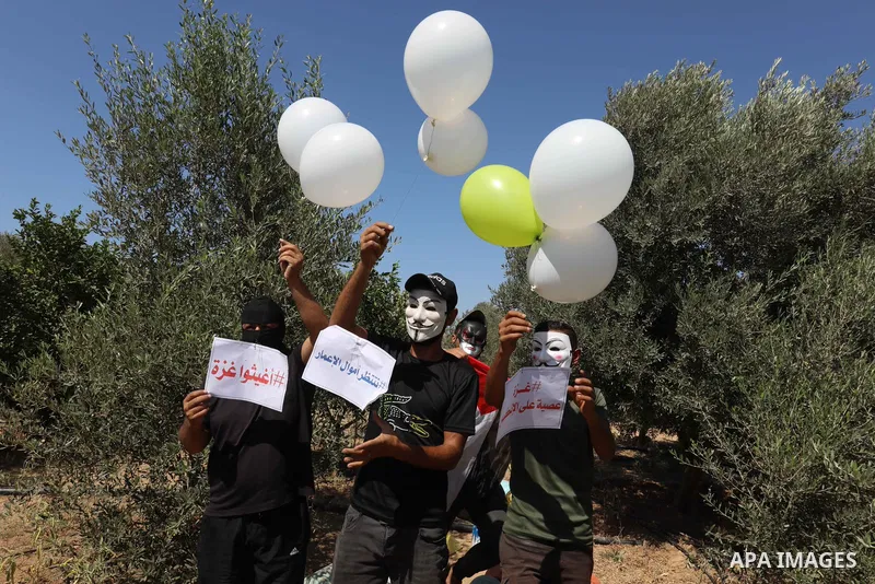 Masked Palestinians prepare incendiary balloons near Jabalia in the northern of Gaza Strip, on September 4, 2021. Reports in Palestinian media indicated that units in charge of incendiary balloon attacks on Israeli plann...