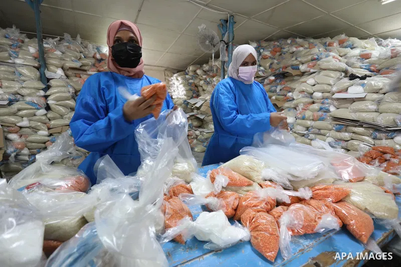Palestinian employees at the United Nations Relief and Works Agency for Palestinian Refugees (UNRWA) wearing protective masks and gloves, prepare food aid rations for refugees, in Dair Al Balah in the center of Gaza stri...