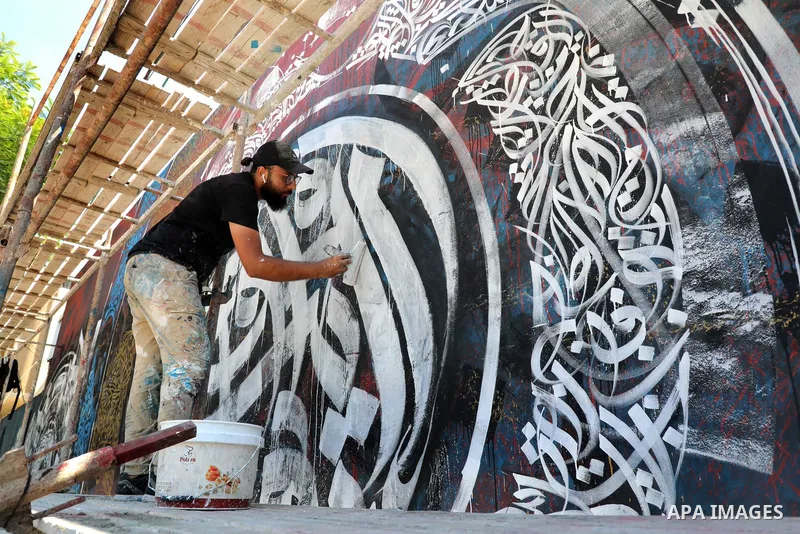 Palestinian artist Bilal Khaled draws on a wall ordinate in Gaza city on July 1, 2021. "Graffiti" (usually both singular and plural) and the rare singular form "graffito" are from the Italian word graffiato ("scratched")...