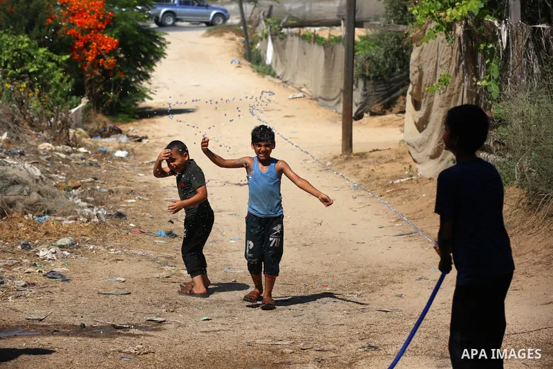 Palestinian children play with water during a hot weather wave, in a slum on the outskirts of the Gaza city on July 01, 2021. Photo by Ashraf Amra