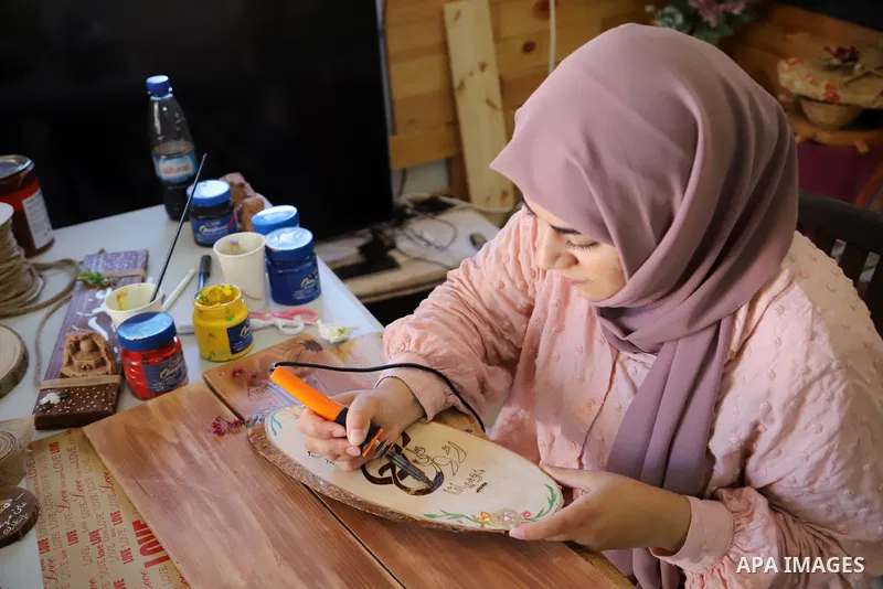 Palestinian artist Majd Abu Haikal, works on wood to makes gifts at her home in the West Bank city of Hebron on July 10, 2021. Abu Haikal works to recycle wood into gifts and paintings. Photo by Ihab Alami