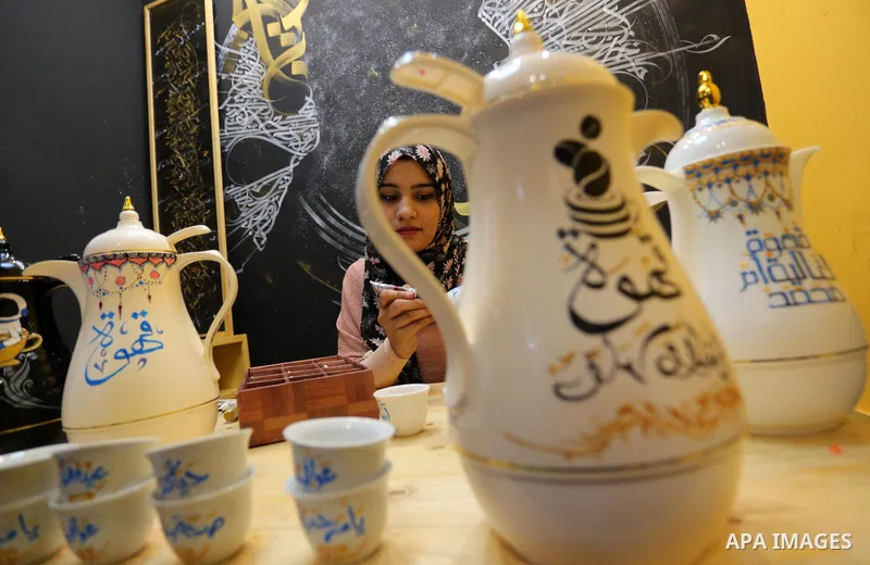 Palestinian artist, Abeer Al-Tallaa, 23, paints on the pots and cups of coffee the congratulatory phrases for Eid Al Fitr, at Maghazi refugee camp in the center of the Gaza Strip, on May 8, 2021. People flock markets and...