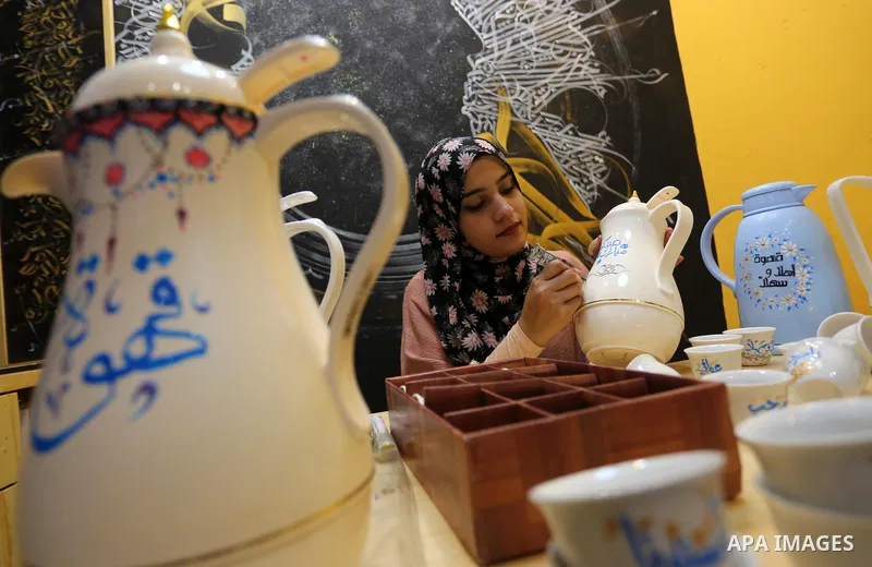 Palestinian artist, Abeer Al-Tallaa, 23, paints on the pots and cups of coffee the congratulatory phrases for Eid Al Fitr, at Maghazi refugee camp in the center of the Gaza Strip, on May 8, 2021. People flock markets and...