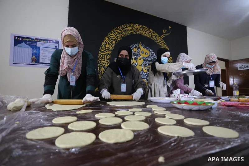 Palestinian deaf girls, wear protective and maskes prepare pastries and pizza for distribution to poor families and latecomers on the roads, during the fasting month of Ramadan, at the Hamm Association, in the Maghazi ca...