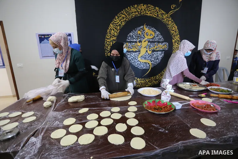 Palestinian deaf girls, wear protective and maskes prepare pastries and pizza for distribution to poor families and latecomers on the roads, during the fasting month of Ramadan, at the Hamm Association, in the Maghazi ca...