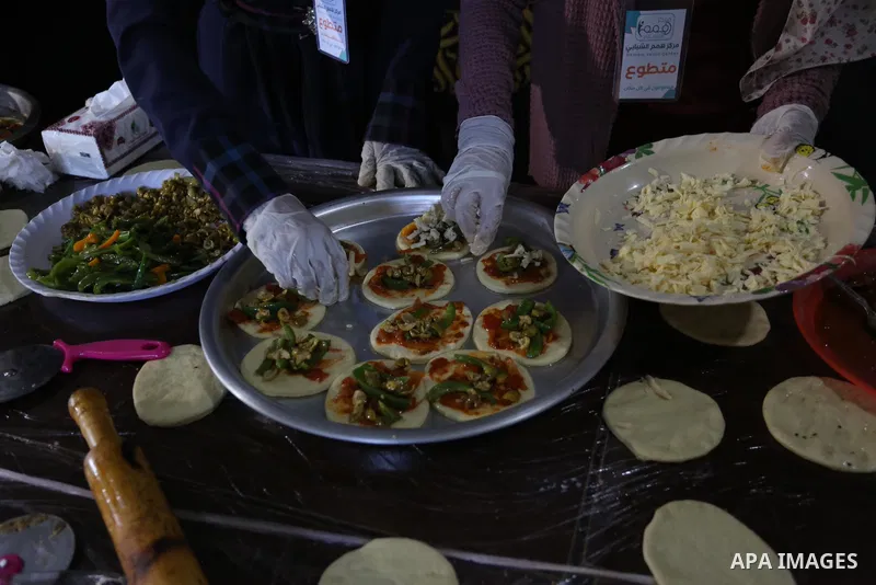 Palestinian deaf girls, wear protective and maskes prepare pastries and pizza for distribution to poor families and latecomers on the roads, during the fasting month of Ramadan, at the Hamm Association, in the Maghazi ca...