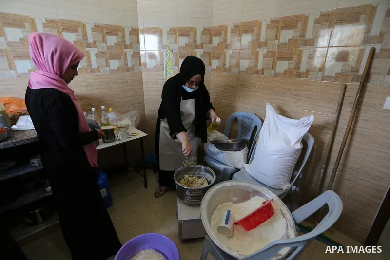 Palestinian deaf girls, wear protective and maskes prepare pastries and pizza for distribution to poor families and latecomers on the roads, during the fasting month of Ramadan, at the Hamm Association, in the Maghazi ca...