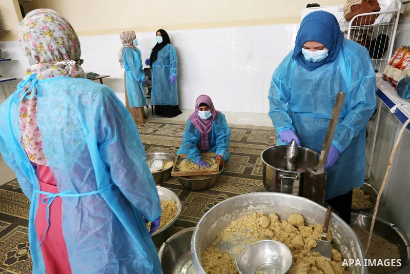 Palestinian women wear protective and maskes prepare traditional food of Couscous "Maftoul", samosa and Kubba in Khan Younis in the southern Gaza Strip, on April 11, 2021 to sell it to customers a head of Islamic holy mo...