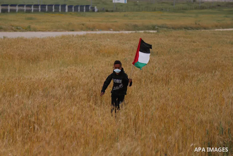Palestinians carry the Palestinian flag near the border with Israel, east of Gaza City on March 30, 2021. Palestinians every year mark Land Day on March 30 commemorating the six Palestinians shot and killed by Israeli po...