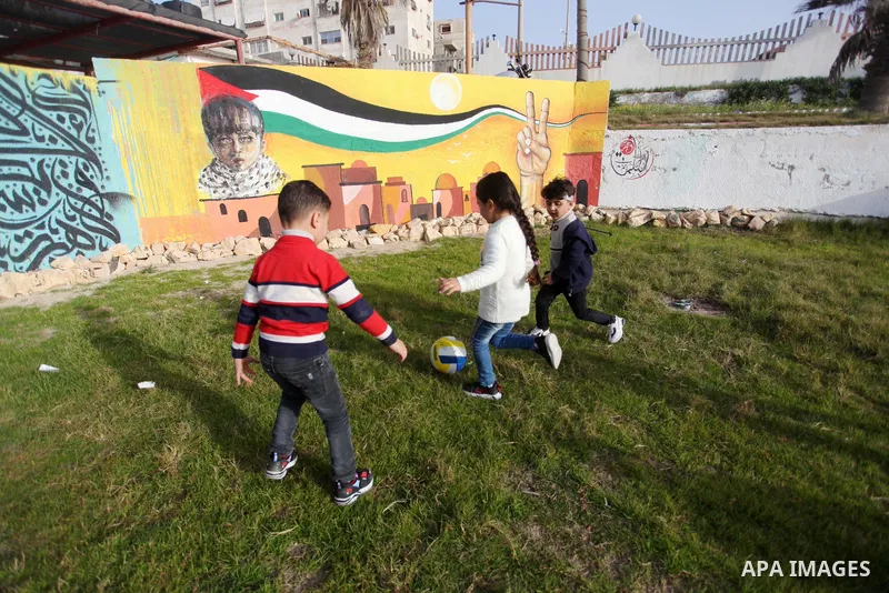 Palestinian children play next to a mural depicting the Palestinian flag in Gaza City on February 2, 2021. Photo by Mahmoud Ajjour