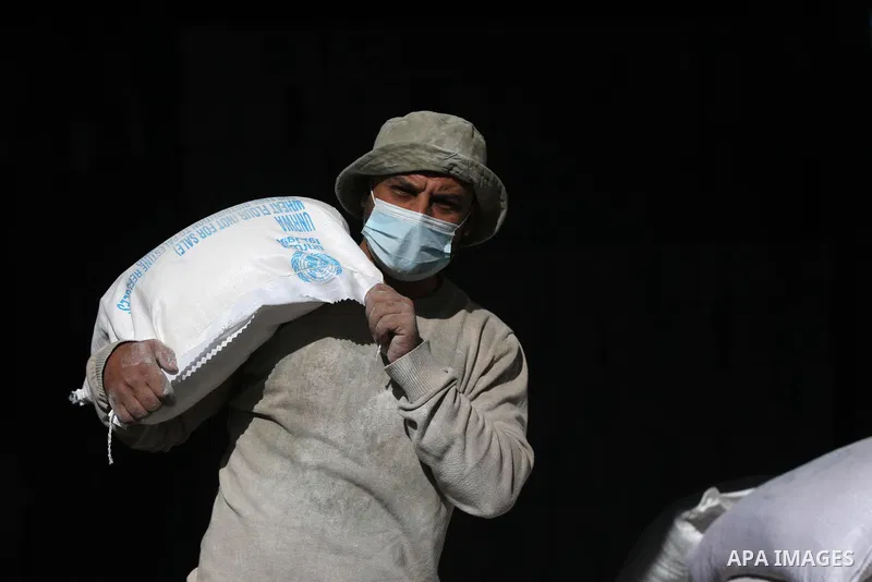 Palestinian workers at the United Nations Relief and Works Agency for Palestinian Refugees (UNRWA) wearing protective masks, transport food aid rations at an aid distribution center, amid the outbreak of the coronavirus...