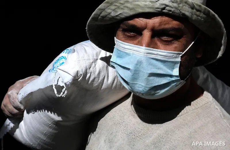 Palestinian workers at the United Nations Relief and Works Agency for Palestinian Refugees (UNRWA) wearing protective masks, transport food aid rations at an aid distribution center, amid the outbreak of the coronavirus...