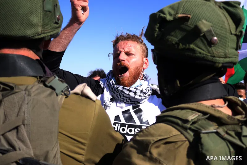 Palestinian protesters hold a Palestinian flag argue with an Israeli soldiers during a protest against the Israeli army and settler attacks targeting the area’s Palestinian residents, in Yatta village in the southern Wes...