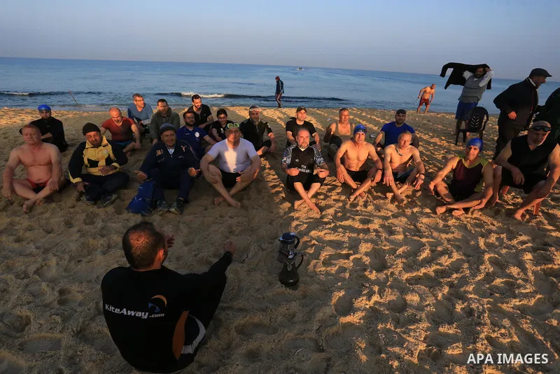 Palestinians warm-up ahead of swimming in the Mediterranean sea during the winter, in Beit Lahia in the northern Gaza Strip, on January 8, 2022. Swimming lovers swim early in the morning during winter in the Mediterranea...