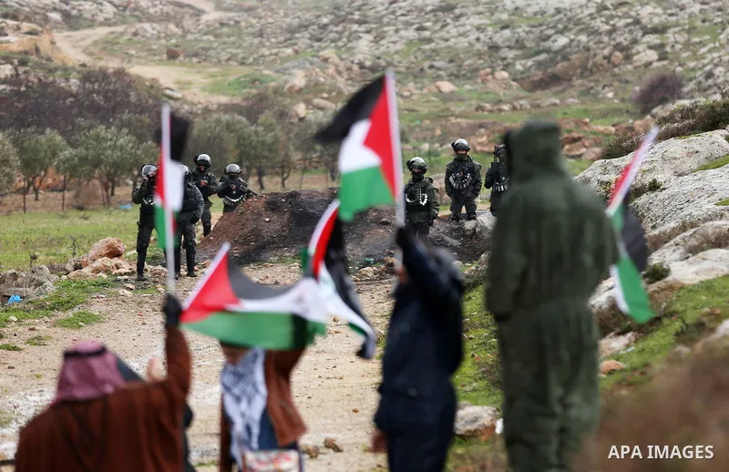 Palestinian protesters hold national flags past Israeli security forces during a demonstration against settlements in the village of Beit Dajan in the West Bank, on January 28, 2022. Photo by Stringer