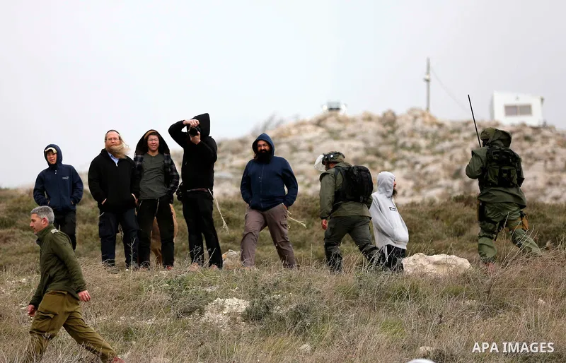 Israeli settlers stand as Palestinians, Israeli activists and members of Knesset plant olive trees near outpost of Givat Ronen in Burin village, near the West Bank city of Nablus on February 4, 2022. Photo by Shadi Jarar...