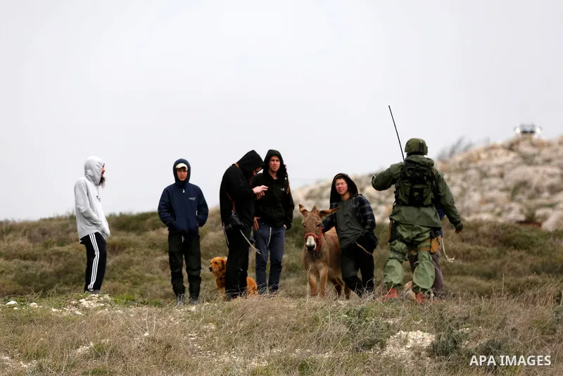 Israeli settlers stand as Palestinians, Israeli activists and members of Knesset plant olive trees near outpost of Givat Ronen in Burin village, near the West Bank city of Nablus on February 4, 2022. Photo by Shadi Jarar...
