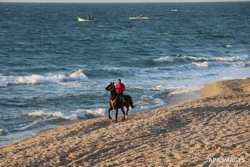 Palestinians are seen on the beach of Deir al-Balah's sea, on February 12, 2022. Generally clear skies are expected today in Palestine with a rise in temperature, which nevertheless remains below the seasonal average, ac...