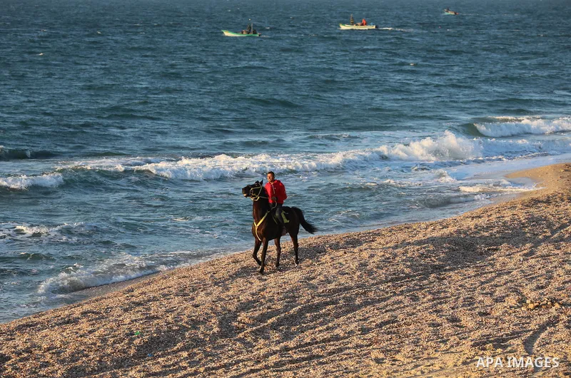 Palestinians are seen on the beach of Deir al-Balah's sea, on February 12, 2022. Generally clear skies are expected today in Palestine with a rise in temperature, which nevertheless remains below the seasonal average, ac...