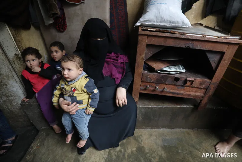 Palestinian woman sits with her children at their home on a rainy day in Deir Al-Balah camp in the central Gaza Strip on February 19, 2022. Poor family consist of 12 members who face difficult life and the high cost of l...