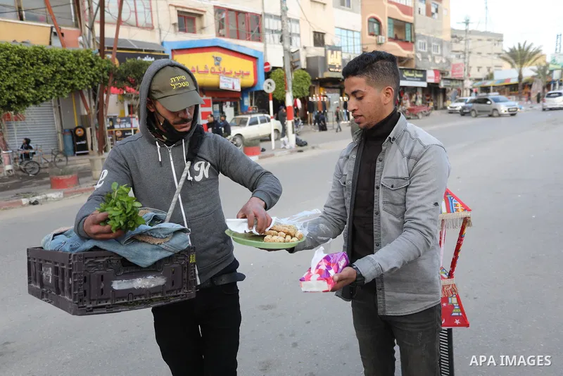 A Palestinian man distribute sweets to people on the street after four Israelis were killed in stabbing and car ramming attack in Beersheba, in Deir al-Balah in the center of Gaza strip on March 22, 2022. Photo by Ashraf...