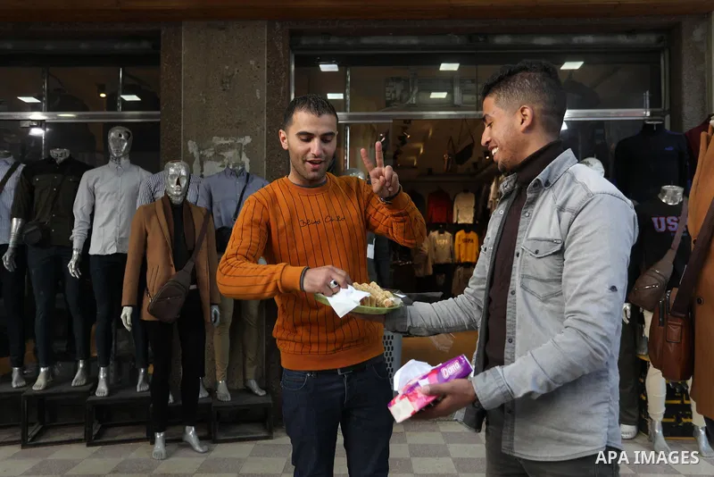 A Palestinian man distribute sweets to people on the street after four Israelis were killed in stabbing and car ramming attack in Beersheba, in Deir al-Balah in the center of Gaza strip on March 22, 2022. Photo by Ashraf...