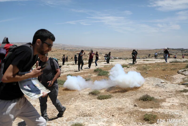Palestinian activists run for cover from tear gas fired by Israeli soldiers during a protest after Israeli top court paved way for razing eight Palestinian hamlets, in Masafer Yatta, south of Hebron, in the West Bank, on...