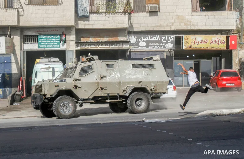 A Palestinian youth throws stones at a military vehicle of the Israeli army, during a military operation for the army to arrest wanted Palestinians in Balata refugee camp in the city of Nablus in the occupied West Bank o...
