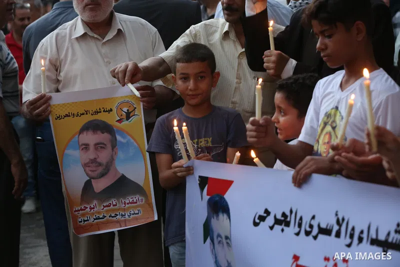 Palestinians hold banners and light candles during a protest in solidarity with Palestinian prisoner in Israeli jails suffering from cancer Nasser Abu Hamid, in front of Red cross office, in Gaza city on September 13, 20...