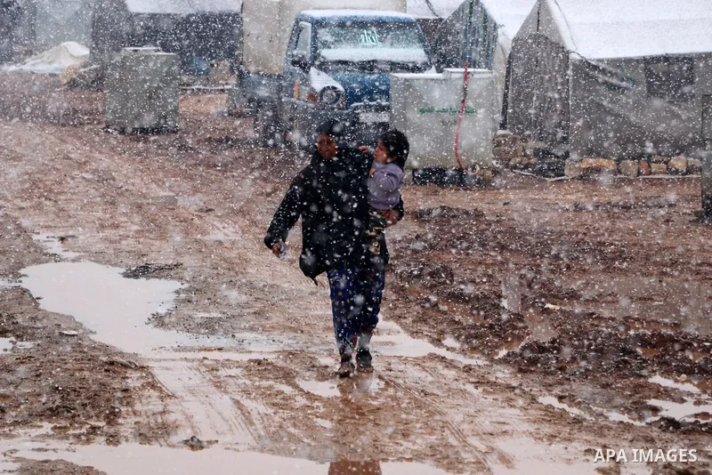 Syrian refugees walk near tents through snow in a camp, outside the Syrian city of Azaz on Syria's northern border with Turkey, on March 13, 2022. Photo by Samir Abed
