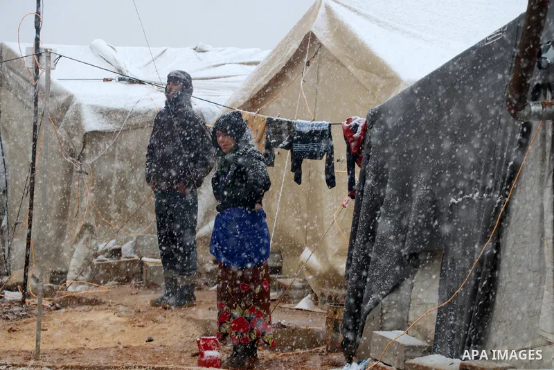 Syrian refugees walk near tents through snow in a camp, outside the Syrian city of Azaz on Syria's northern border with Turkey, on March 13, 2022. Photo by Samir Abed