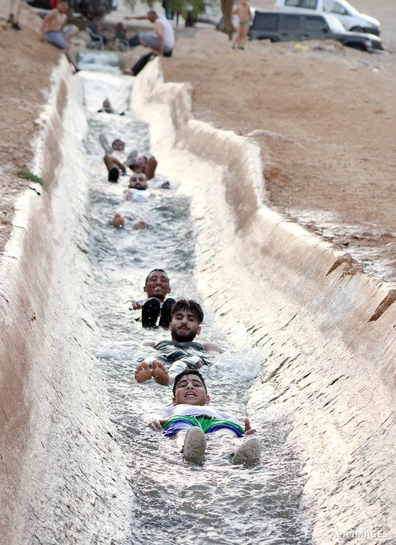 Palestinians slide down a water canal in al-Auja village of the Jordan Valley, in the West Bank on August 24, 2023, during high summer heat in the region. Photo by Mohammad Jawad\ apaimages
