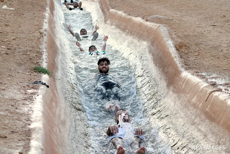 Palestinians slide down a water canal in al-Auja village of the Jordan Valley, in the West Bank on August 24, 2023, during high summer heat in the region. Photo by Mohammad Jawad\ apaimages