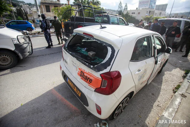 People gather around a car which was destroyed by Palestinian youth in the West Bank city of Nablus on March 18, 2023. According to local source, inside the car were Israeli settlers, while Israeli media said that the ca...