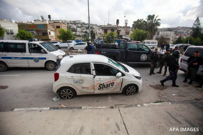 People gather around a car which was destroyed by Palestinian youth in the West Bank city of Nablus on March 18, 2023. According to local source, inside the car were Israeli settlers, while Israeli media said that the ca...