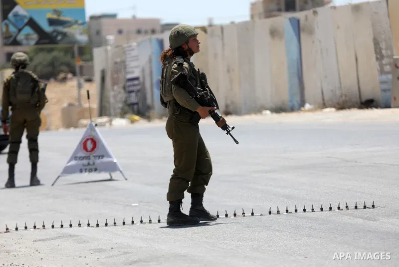 Israeli soldiers block the road leading to the West Bank town of Janatah south of Bethlehem, as settlers wave flags, following a reported shooting attack at the Tekoa junction on July 16, 2023. Israeli forces blocked the...