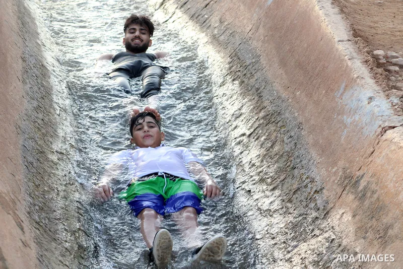 Palestinians slide down a water canal in al-Auja village of the Jordan Valley, in the West Bank on August 24, 2023, during high summer heat in the region. Photo by Mohammad Jawad\ apaimages