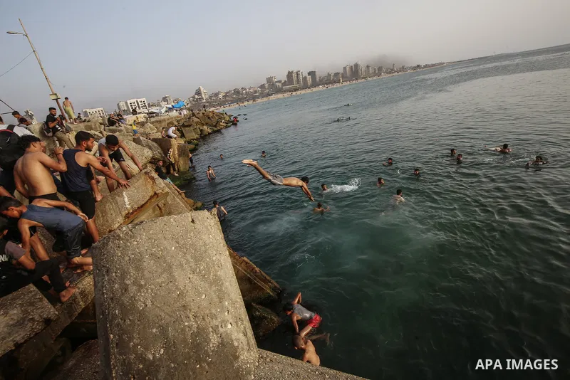 Palestinians, struggling with harsh living conditions due to ongoing Israeli attacks on the Gaza Strip and an intensifying heatwave, gather on the coast to cool off, spending the evening hours by the seaside to escape th...