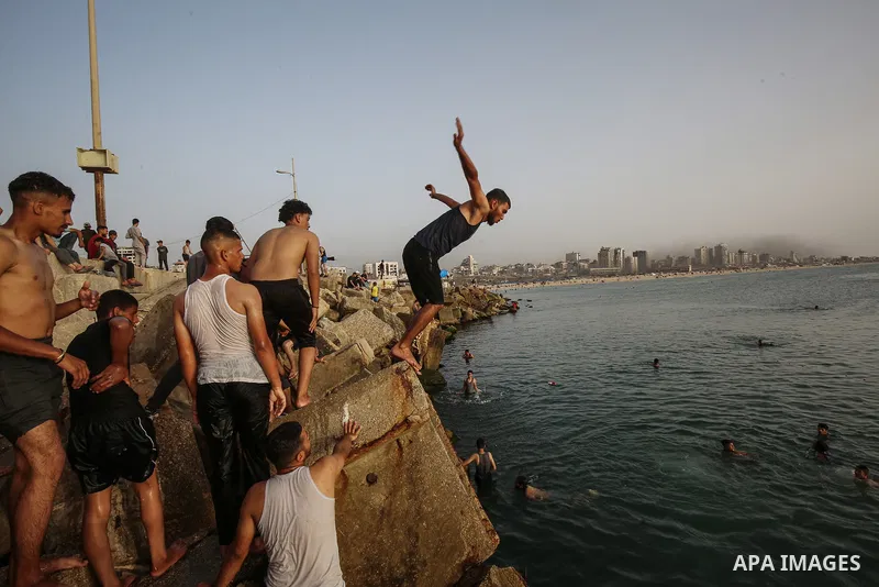 Palestinians, struggling with harsh living conditions due to ongoing Israeli attacks on the Gaza Strip and an intensifying heatwave, gather on the coast to cool off, spending the evening hours by the seaside to escape th...