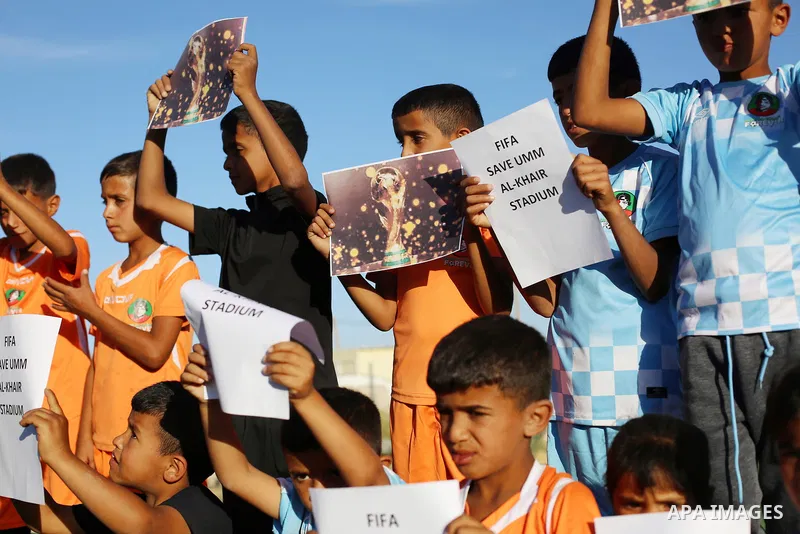 Children hold placards at a playground threatened with demolition in the village of Umm al-Khair, south of Hebron in the West Bank, on June 11, 2026. The children sent a message to FIFA at the start of the World Cup, cal...