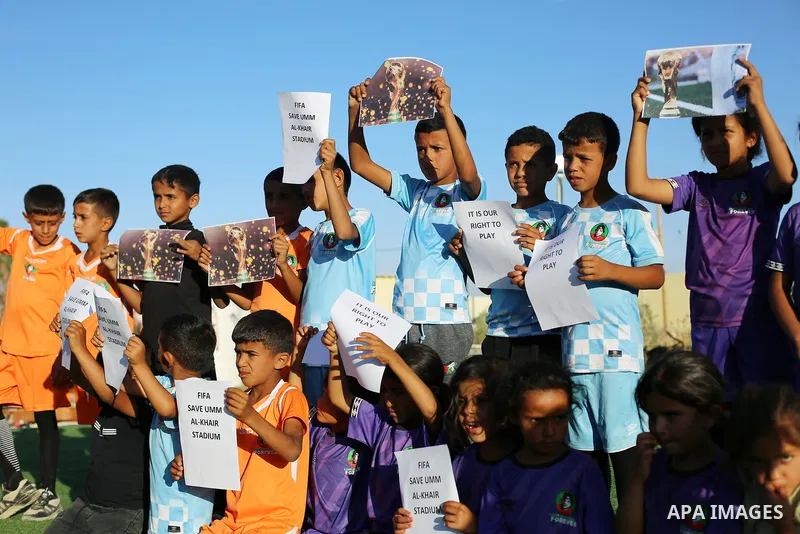 Children hold placards at a playground threatened with demolition in the village of Umm al-Khair, south of Hebron in the West Bank, on June 11, 2026. The children sent a message to FIFA at the start of the World Cup, cal...