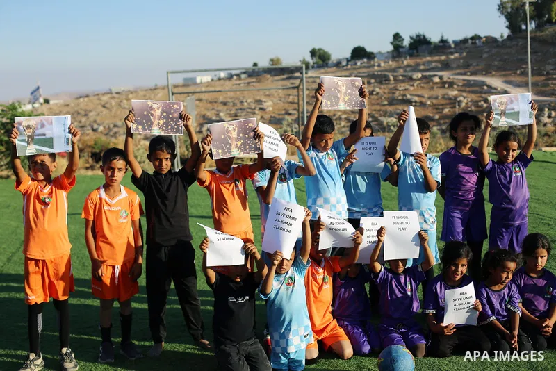 Children hold placards at a playground threatened with demolition in the village of Umm al-Khair, south of Hebron in the West Bank, on June 11, 2026. The children sent a message to FIFA at the start of the World Cup, cal...
