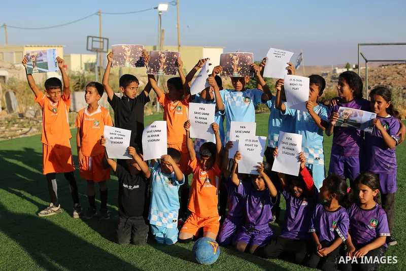 Children hold placards at a playground threatened with demolition in the village of Umm al-Khair, south of Hebron in the West Bank, on June 11, 2026. The children sent a message to FIFA at the start of the World Cup, cal...