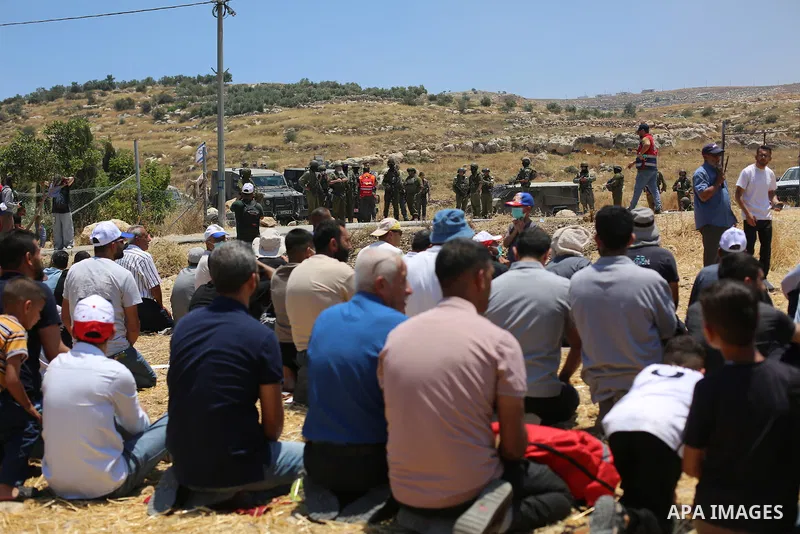 Israeli security forces stand guard as Palestinian men, who had gathered to protest threats of confiscation of their land, perform the Muslim Friday noon prayers in a field in the village of Idna, west of Hebron in the o...