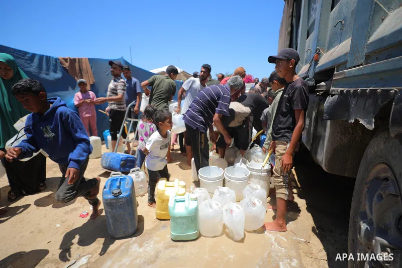 Palestinian women and children stand in line to collect drinking water in the al-Zawaida area of the central Gaza Strip, on June 18, 2026. Residents continue to face severe shortages of clean water amid extreme summer te...