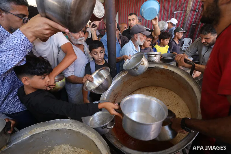 Displaced Palestinians gather to receive food meals from a charitable kitchen in the Nuseirat refugee camp in the central Gaza Strip, on July 12, 2026, amid the ongoing displacement crisis and shortages of humanitarian s...